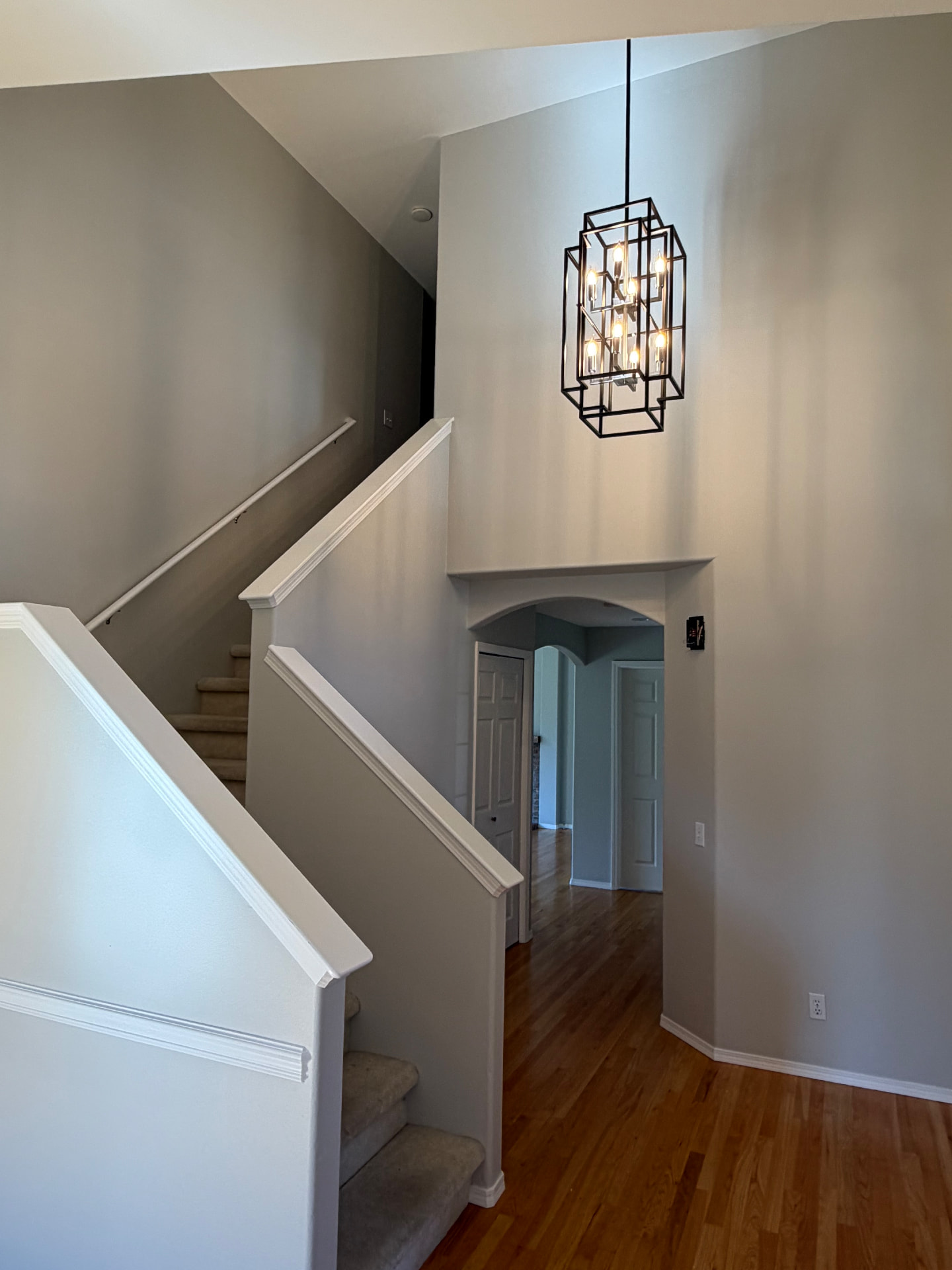 Black geometric chandelier illuminated in a tall residential stairwell