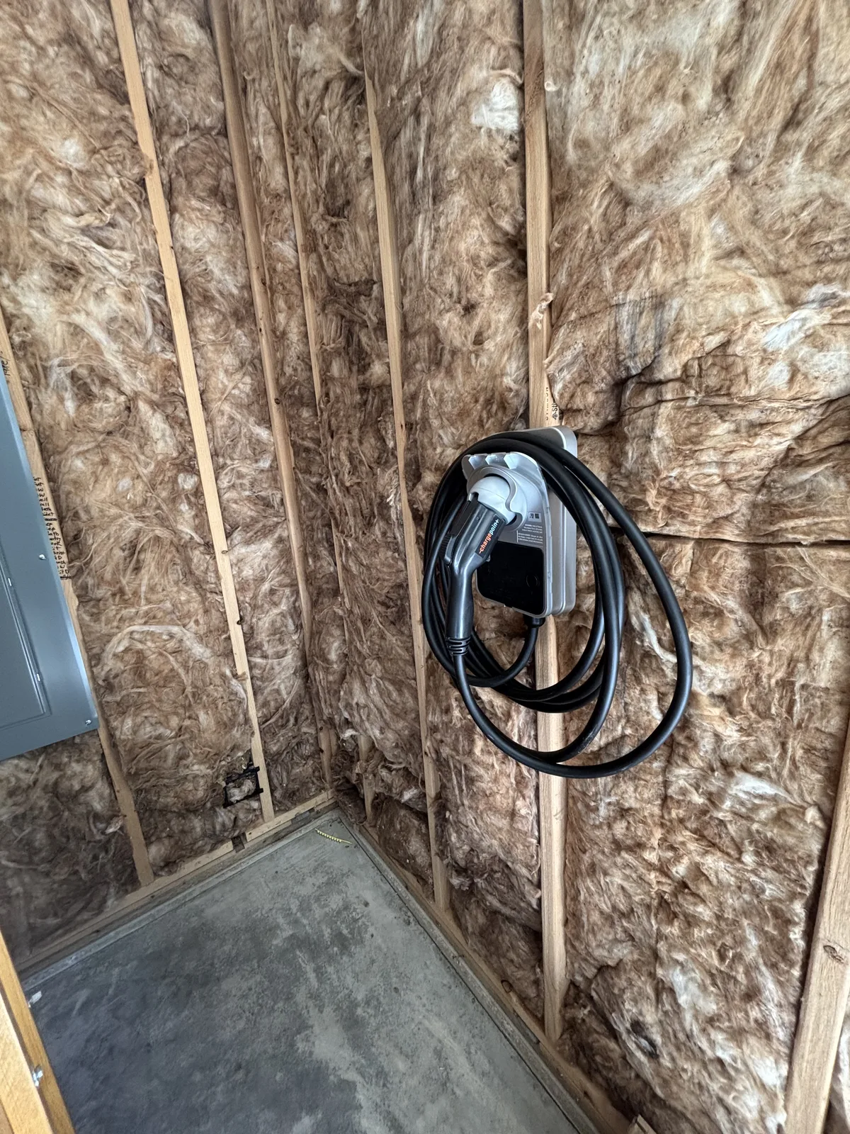 EV charging cable hung on a wall-mounted charger in an insulated unfinished garage
