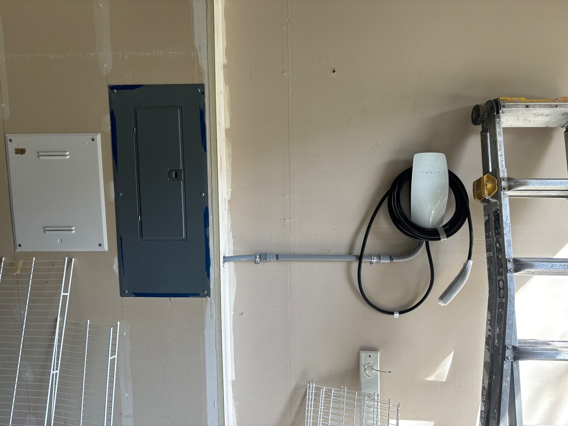 Tesla Wall Connector connected by surface-mounted conduit to a garage electrical panel