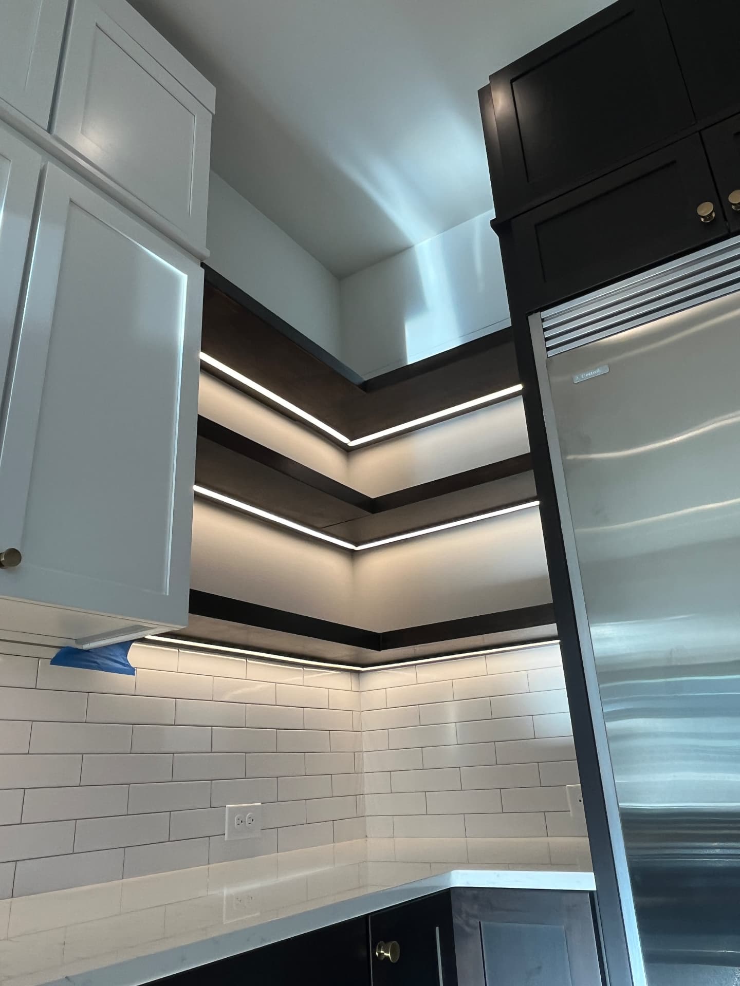 Linear LED lighting beneath dark floating kitchen shelves