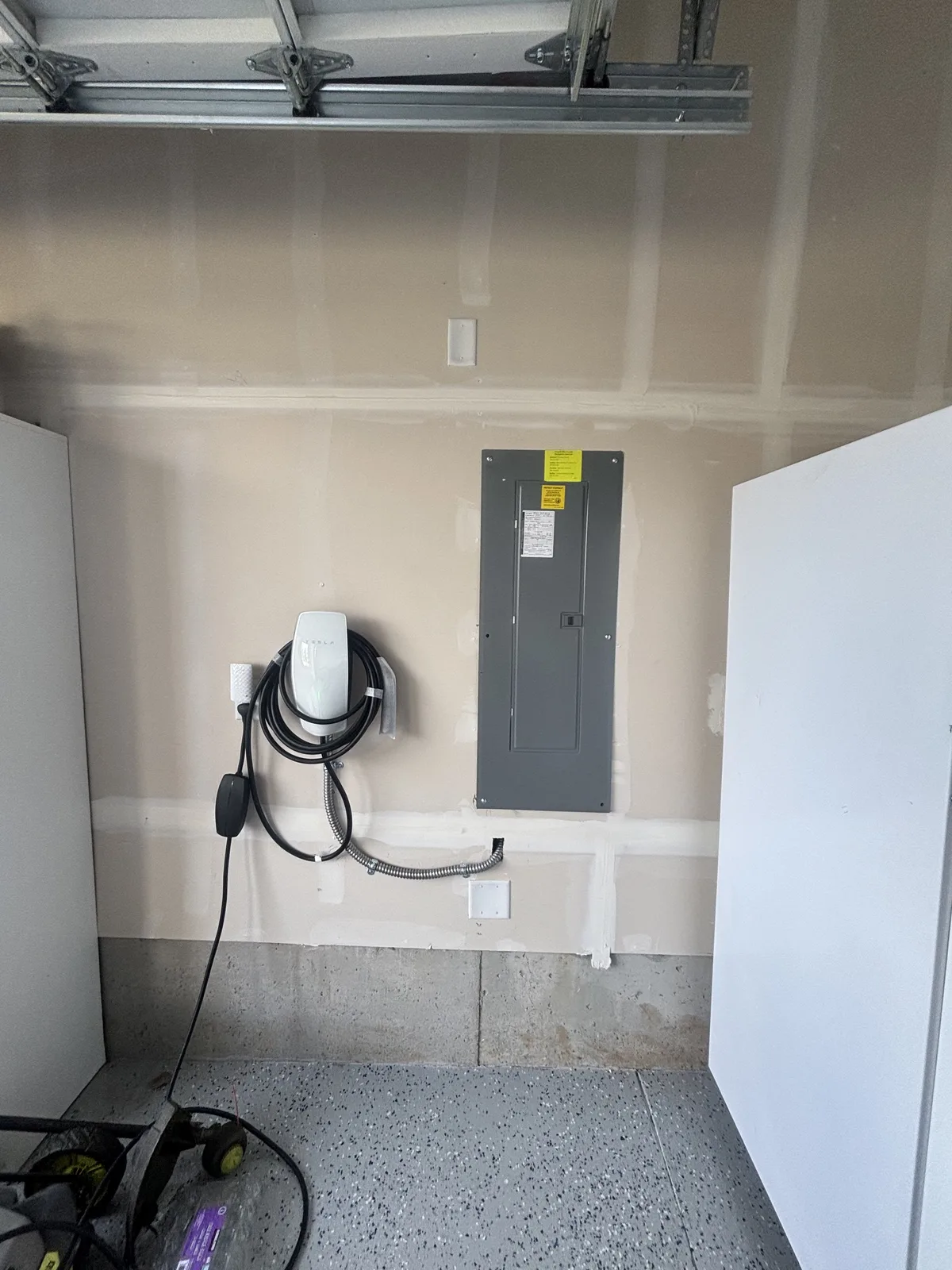 White EV charger mounted beside a closed gray electrical panel in a garage