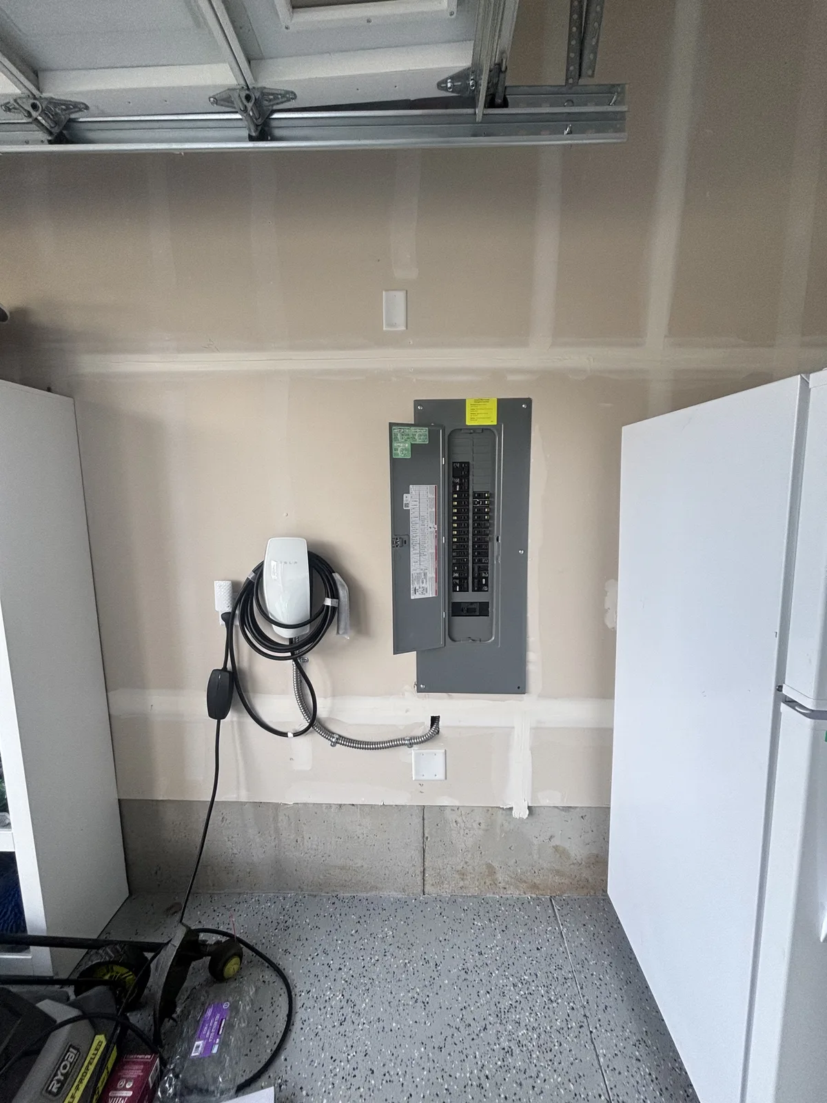 Garage EV charger beside an open electrical panel showing the installed breakers